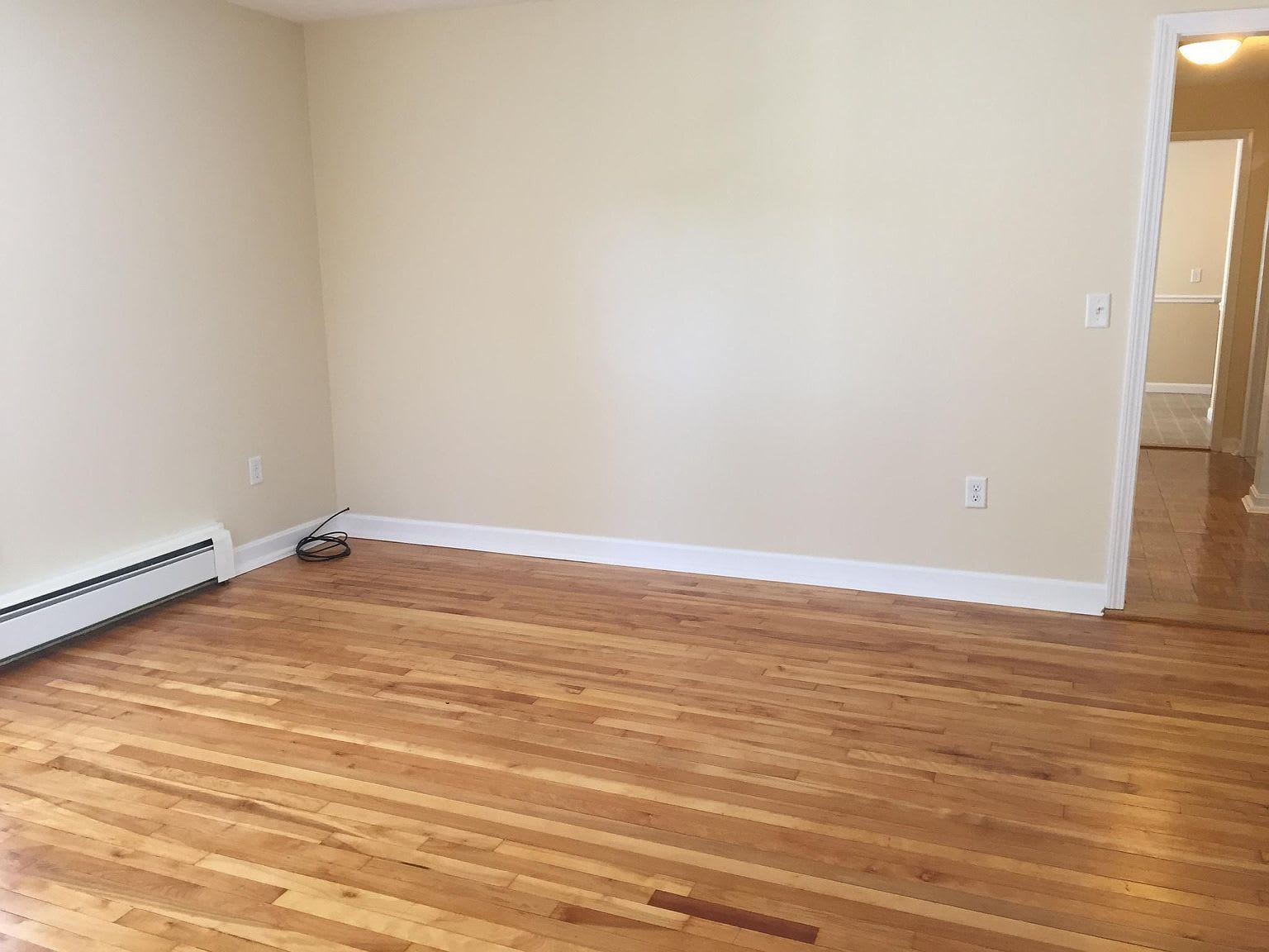 Empty room with hardwood floors, beige walls, and a doorway to another room.