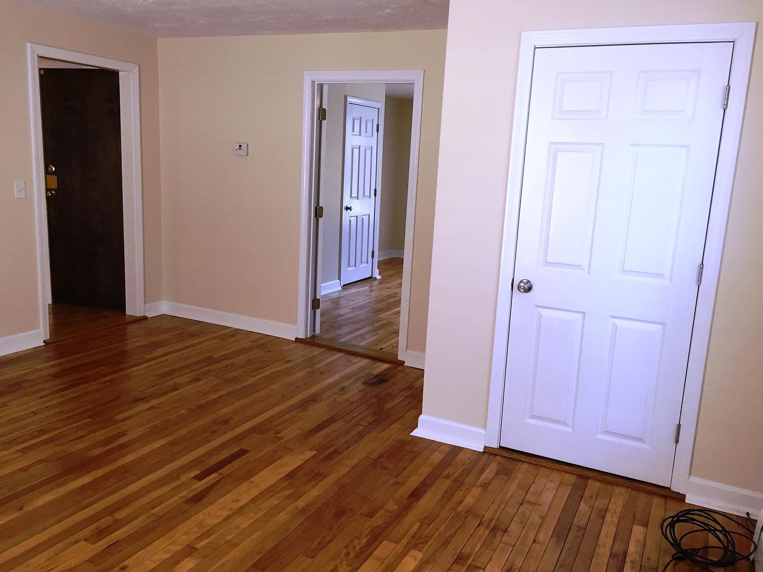 Empty room with wood floors, three doorways, and white trim.
