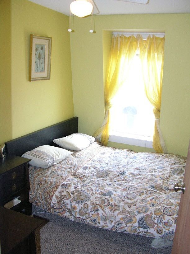 Small bedroom with yellow walls, a bed, and a window with yellow curtains.