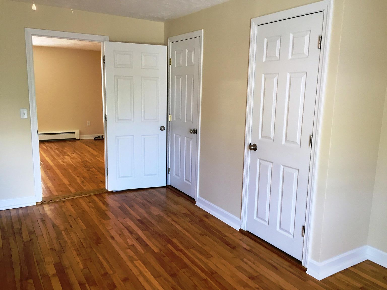 Empty room with hardwood floors, two white doors, and an open doorway to another room.