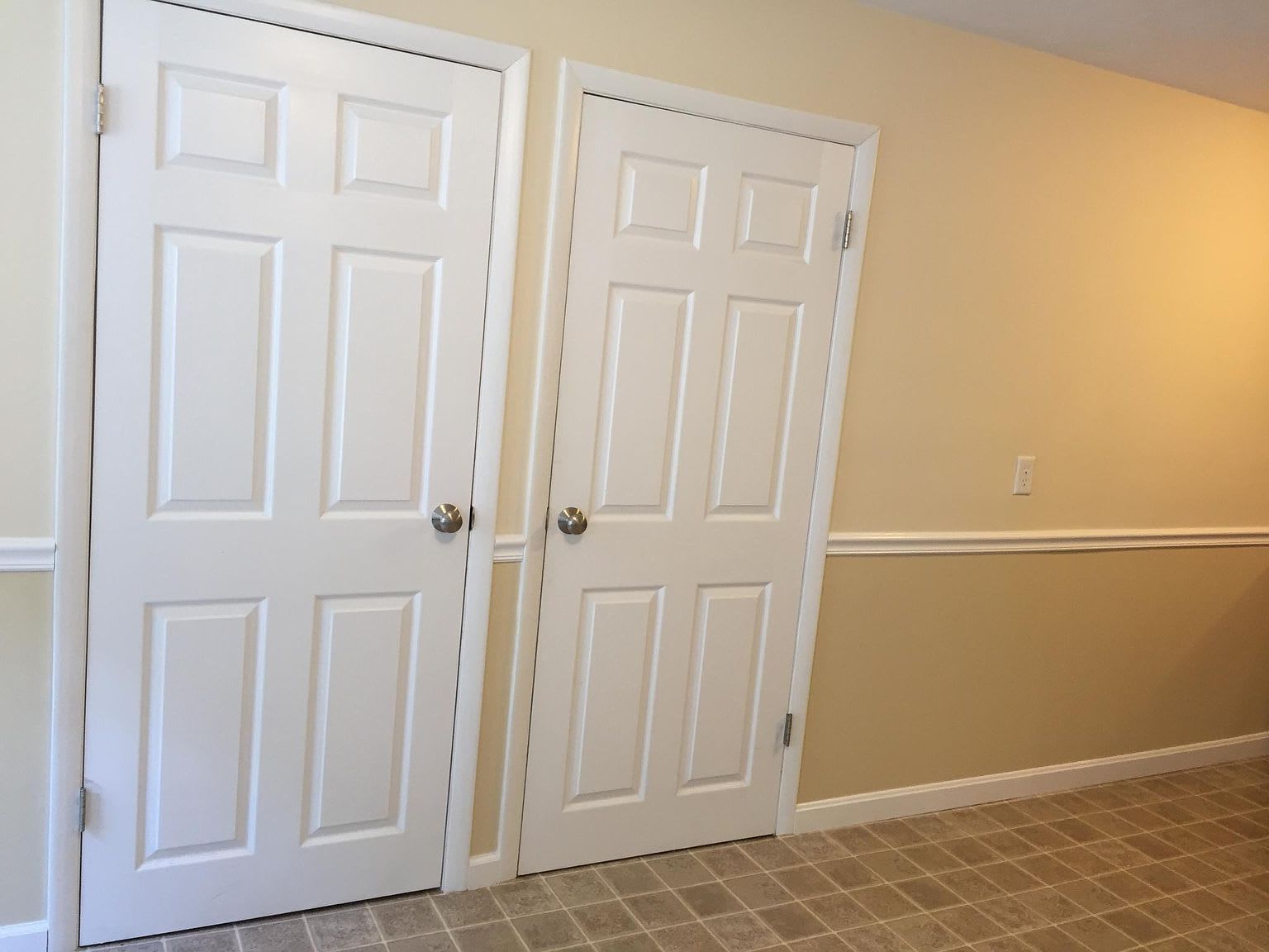 Two white panel doors in a beige room with carpet and a chair rail.