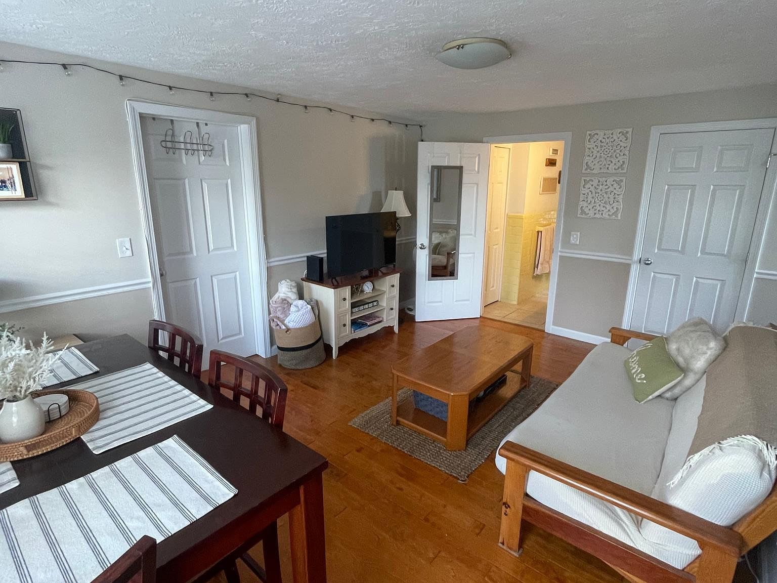Cozy living room with dining table, TV, futon, wooden floors, and white doors.