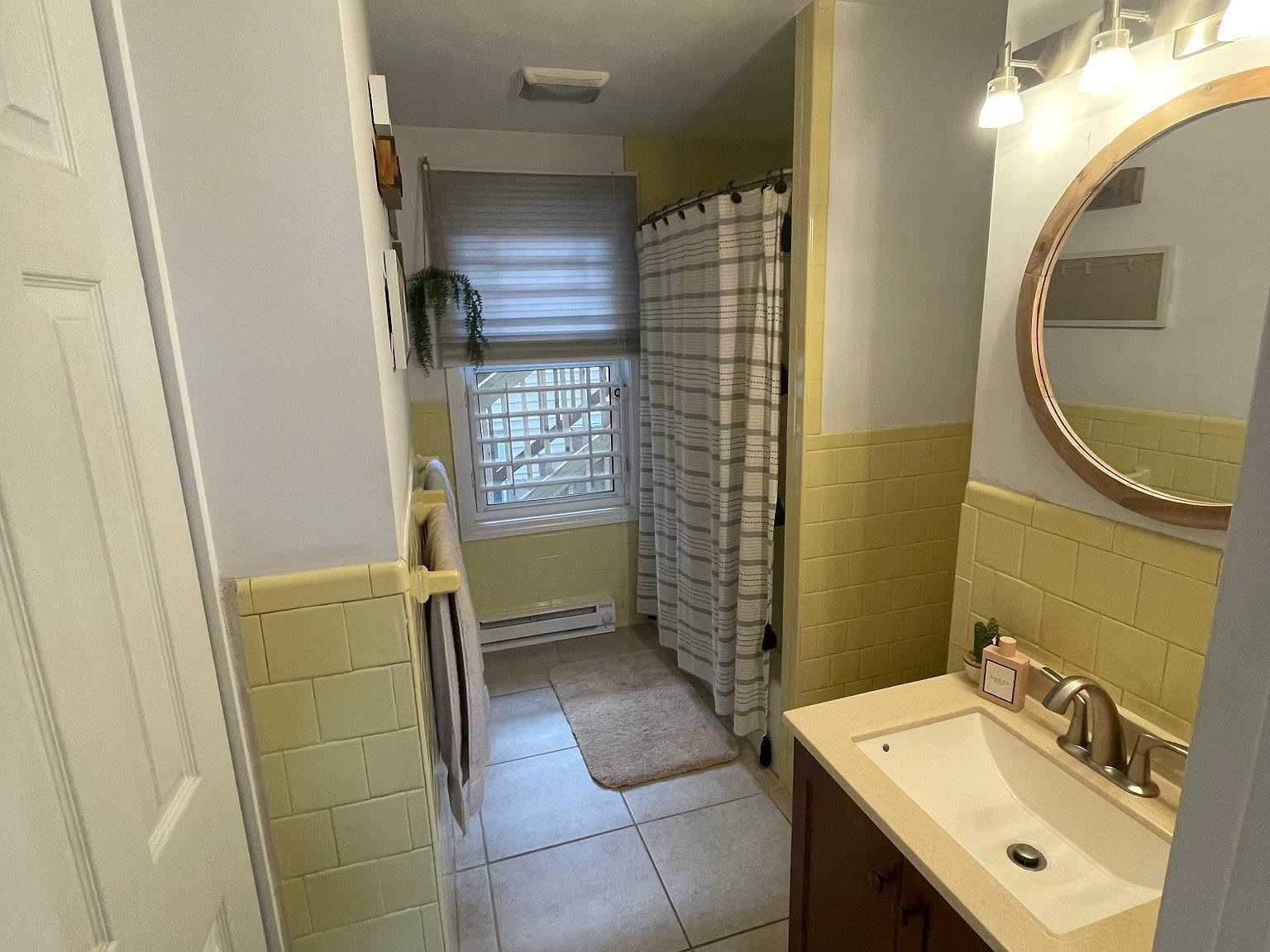 Bathroom with yellow tile, shower curtain, and a vanity with a round mirror.
