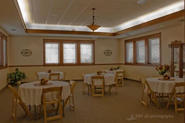 A banquet hall with round tables covered in white cloths, windows, and decorative light fixtures.