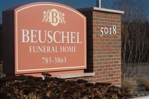 Sign for Beuschel Funeral Home, peach-colored with white text, and brick pillar with address 5018.