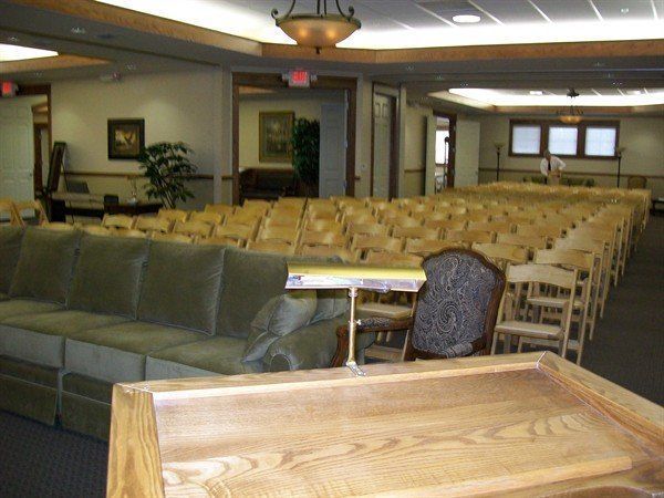 Auditorium interior with rows of wooden chairs, a sofa, and a lectern.