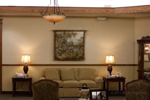 Cozy waiting area with sofa, lamps, tapestry, and cabinet; beige walls and wood trim.