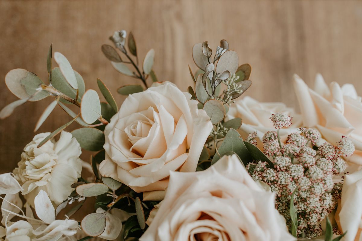 Close-up of a bouquet with light-colored roses, greenery, and small flowers against a neutral background.