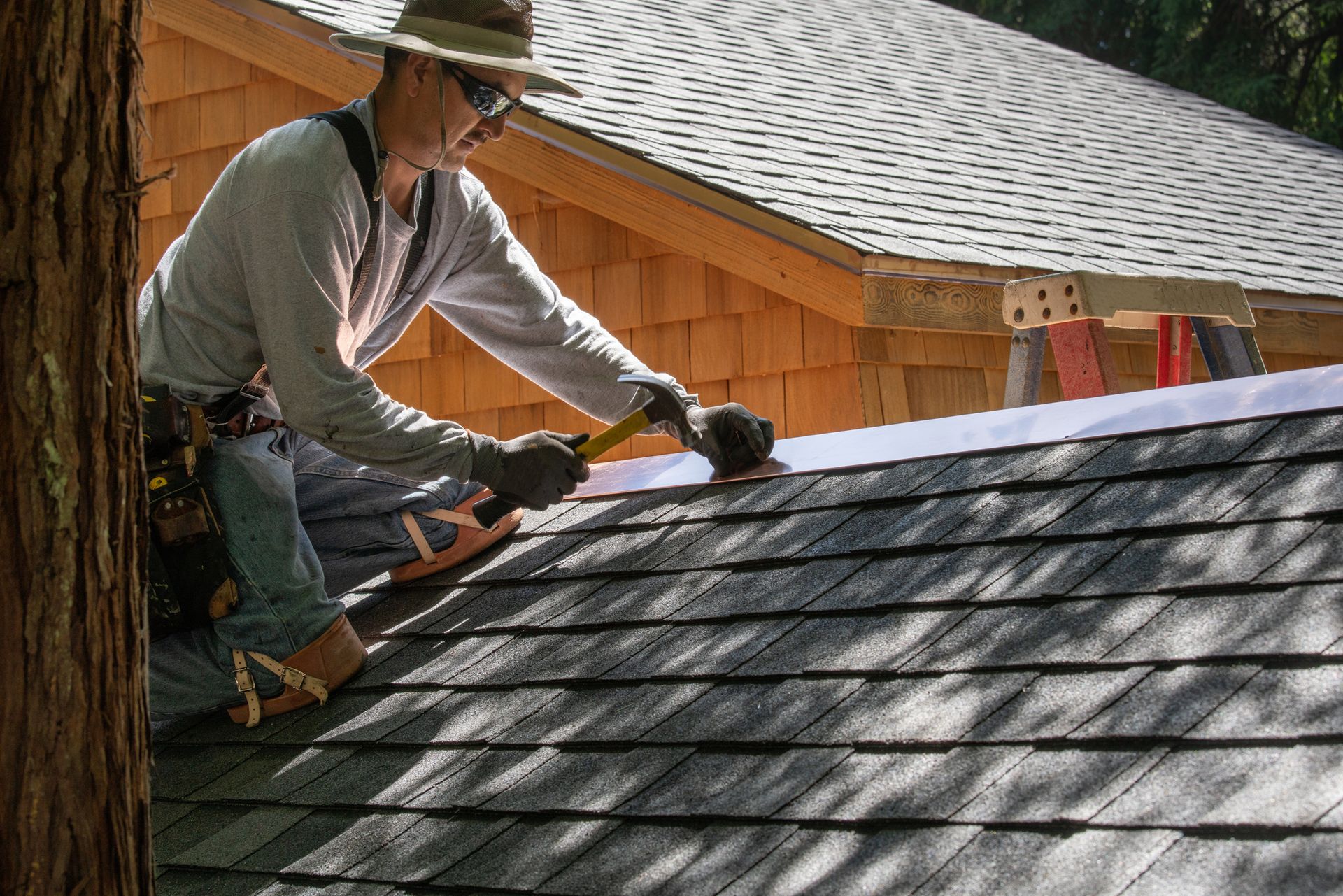 A roofing contractor, in protective gear, is installing a new roof with a hammer and copper edge.