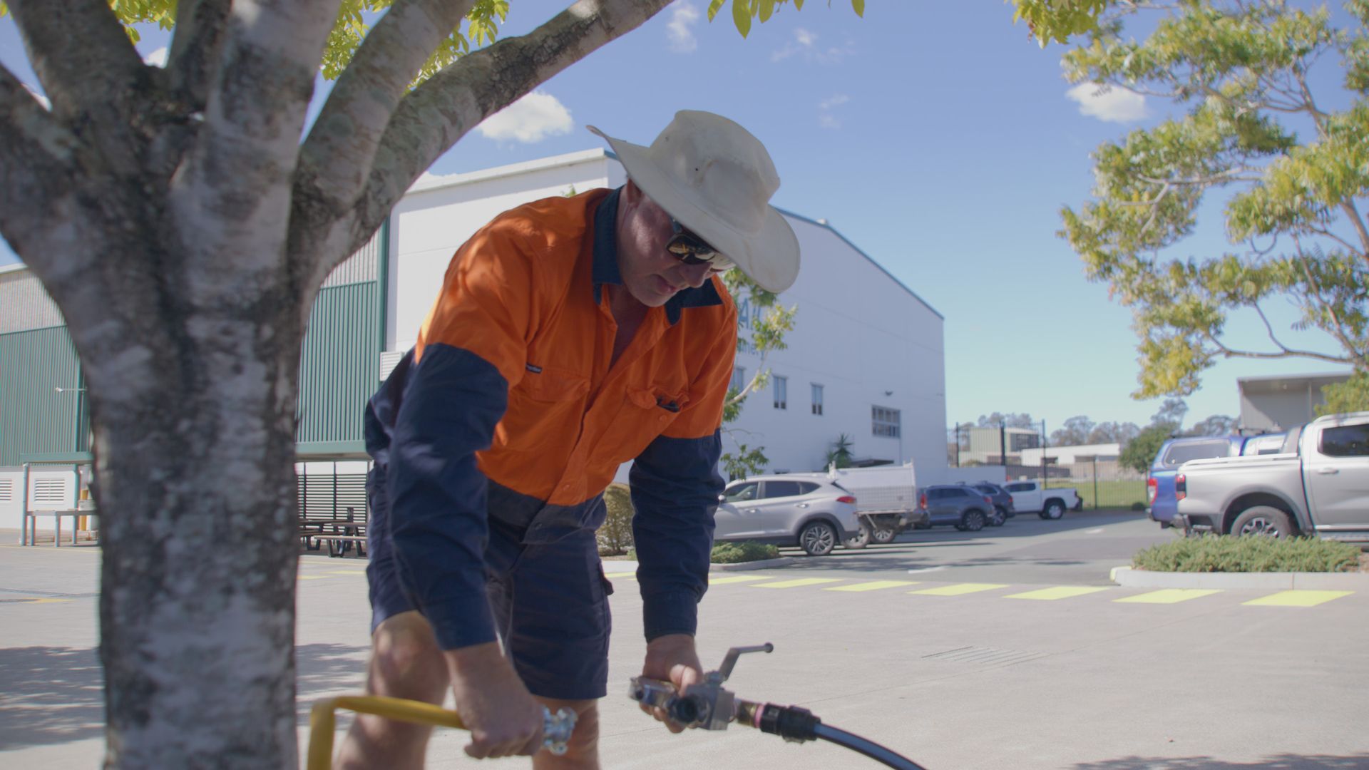 Man in orange work shirt and hat leans over, using a hose outdoors. — Commercial Leak Detection in Goodna, QLD