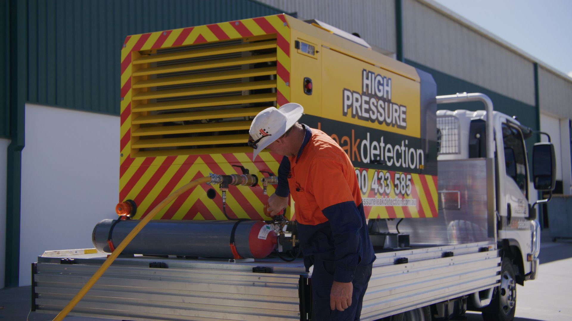 Man in work attire inspecting equipment on a truck bed; yellow and red high-pressure leak detection machine.