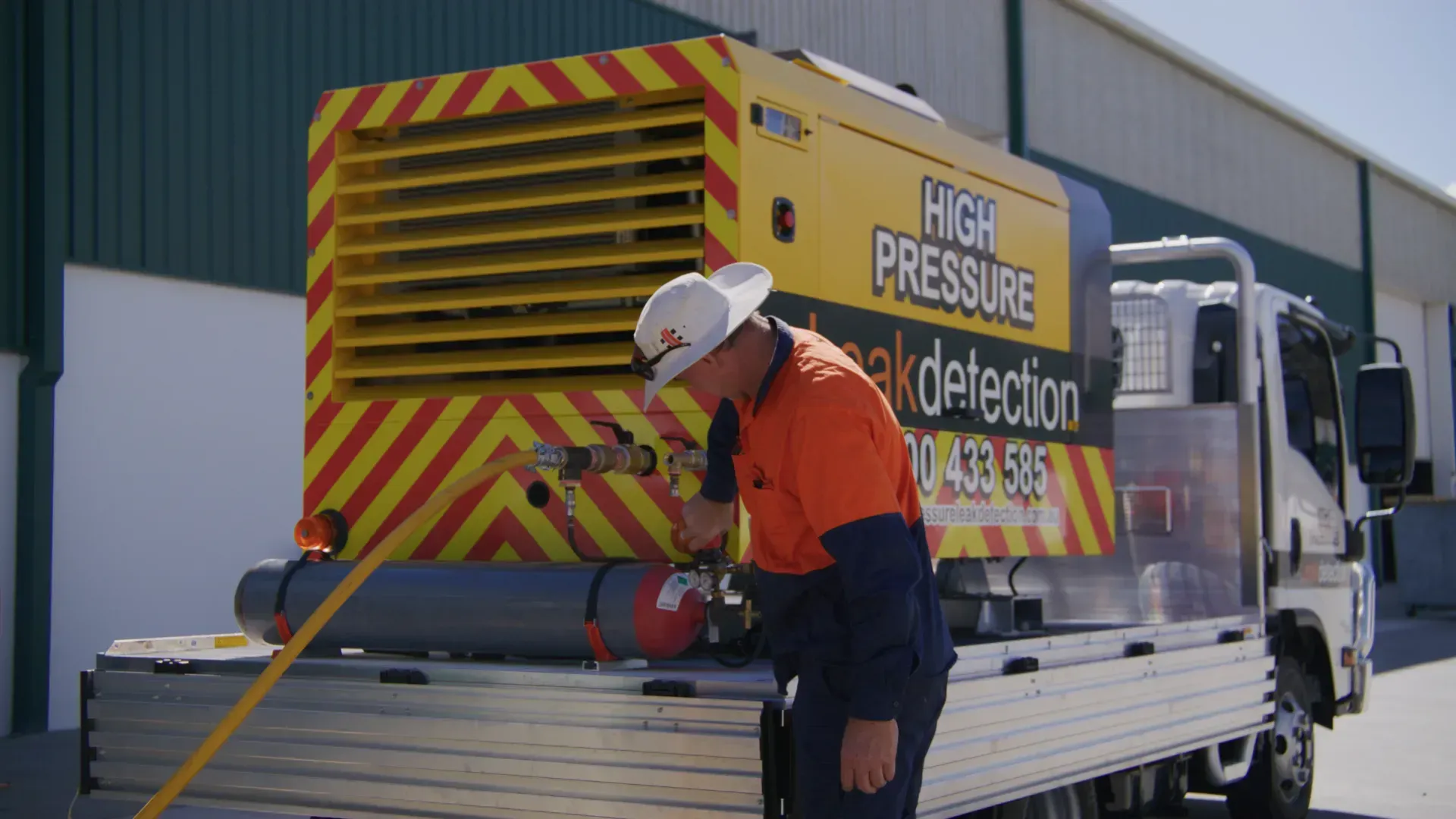 A worker in an orange shirt inspects high-pressure leak detection equipment on a truck bed. — Commercial Leak Detection