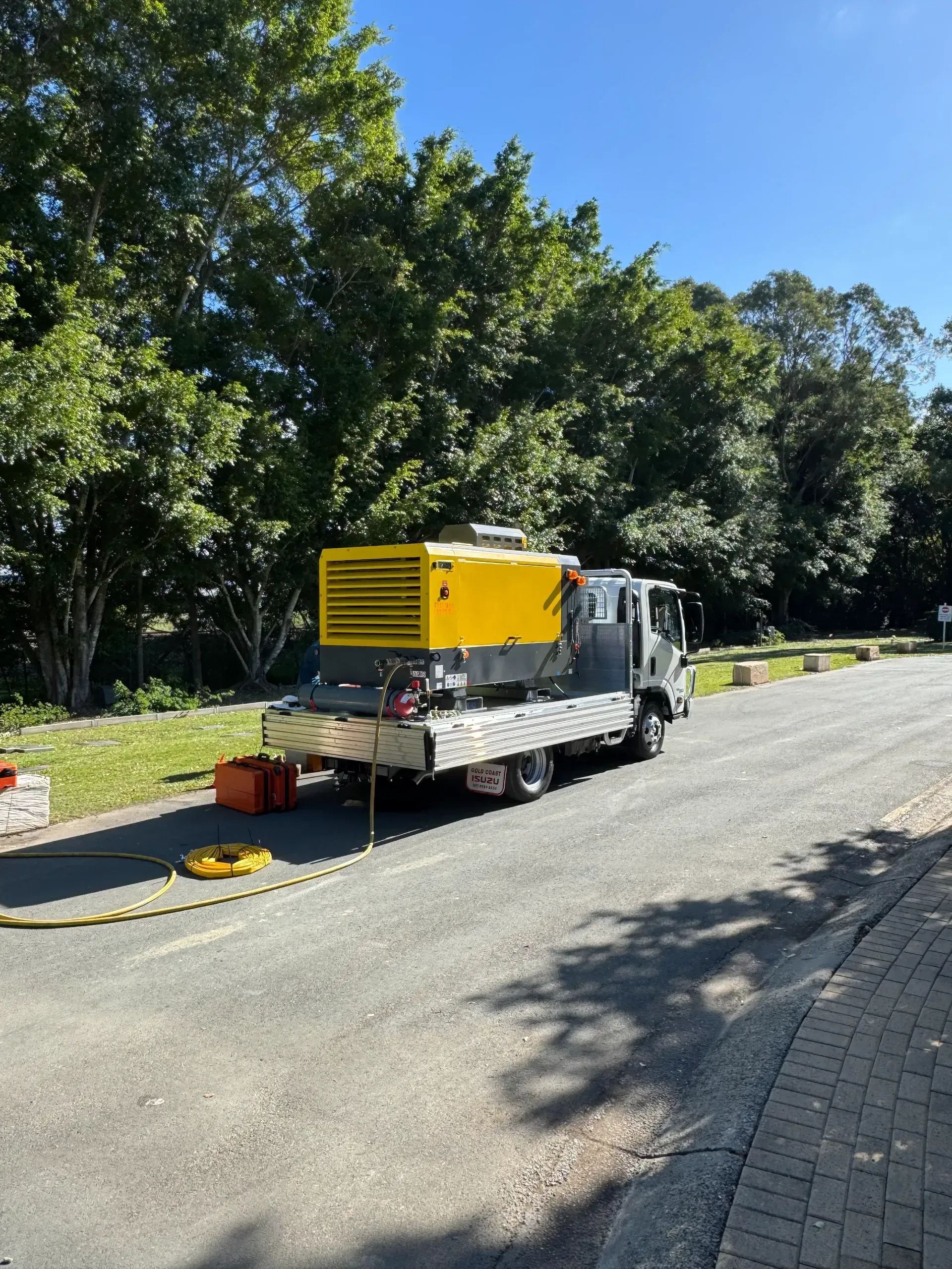 Yellow generator on a truck parked on a paved road next to green trees.  — Commercial Leak Detection