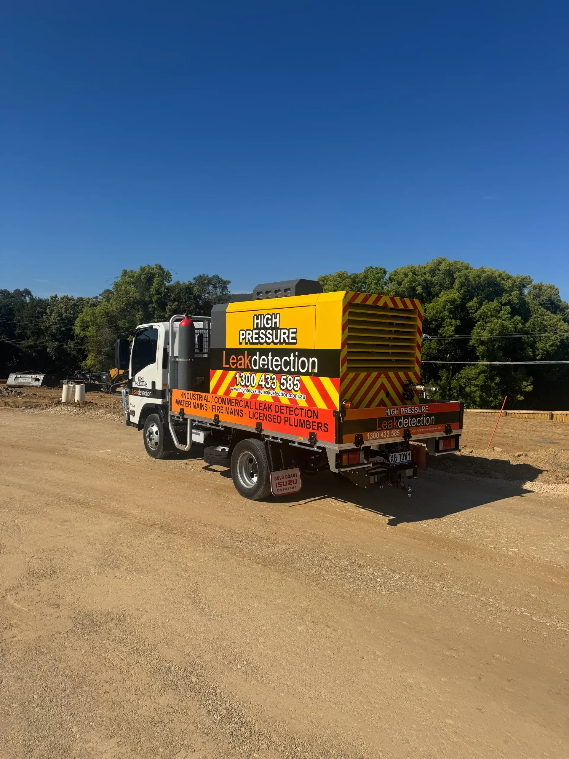 White truck with yellow machinery on the back, parked on a gravel road, blue sky.  — Commercial Leak Detection