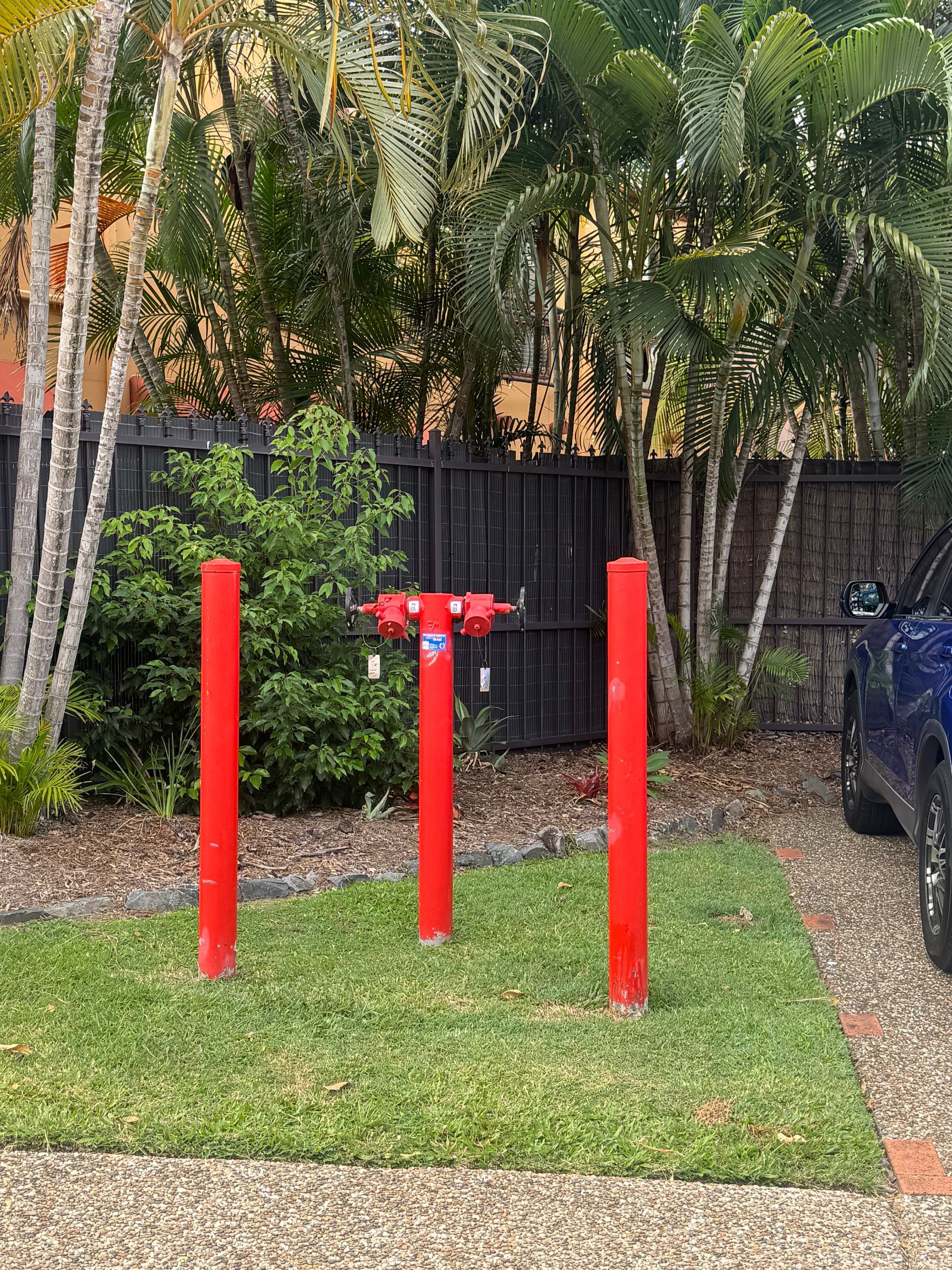 Red Fire Hydrant and Posts on Green Grass — Commercial Leak Detection in Mudgeeraba, QLD