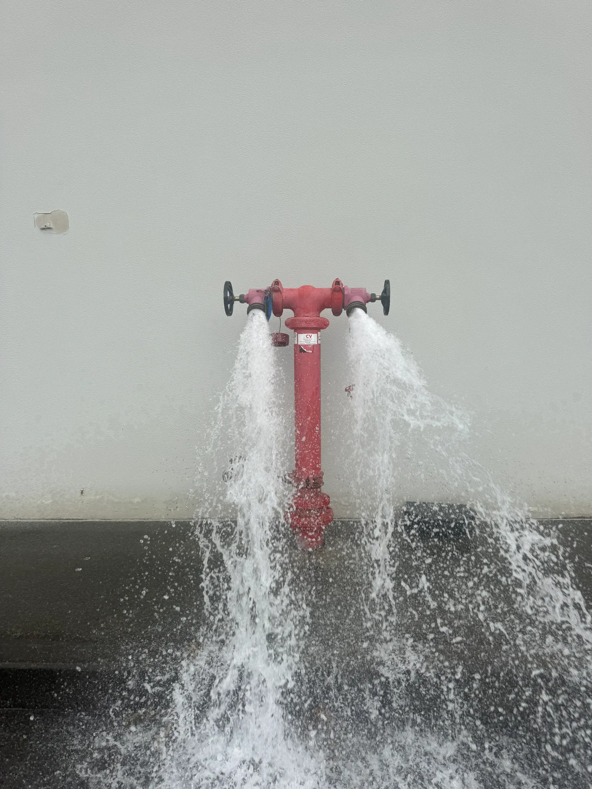 Red fire hydrant sprays water against a white wall.  — Commercial Leak Detection