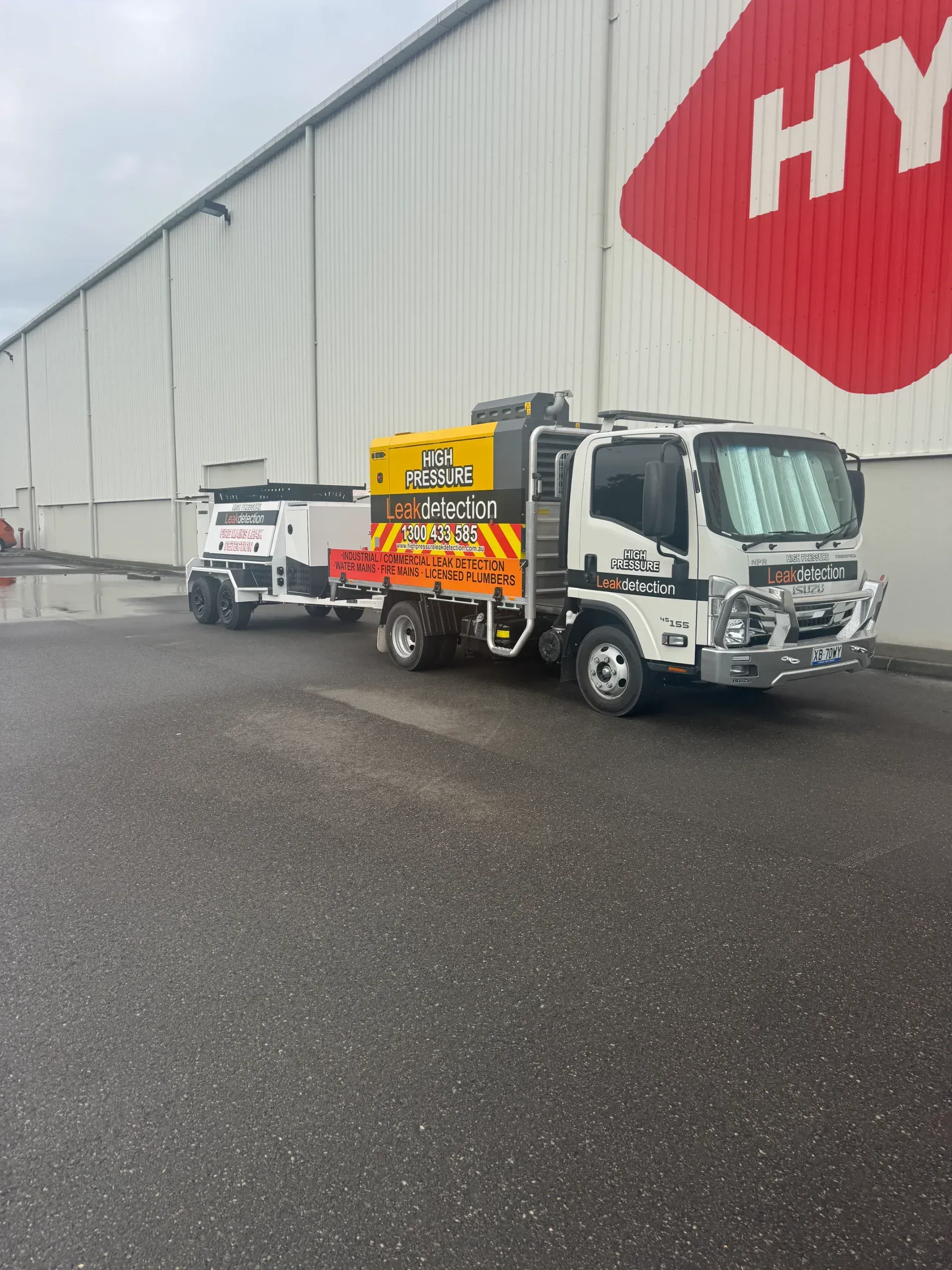 Truck with trailer in front of a white building with a red logo.