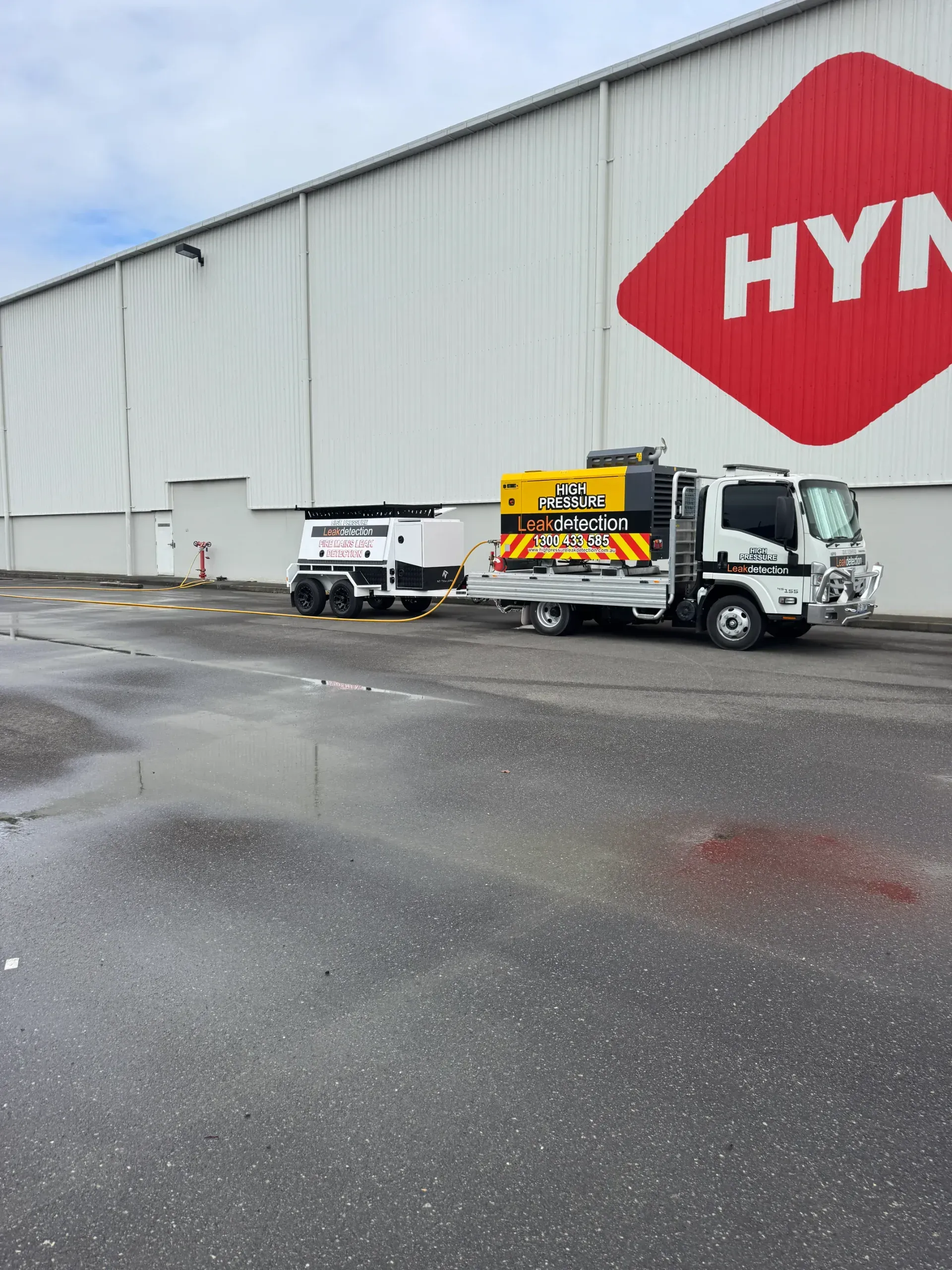 Truck with attached trailer parked in front of a white building with a red HYN logo.  — Commercial Leak Detection