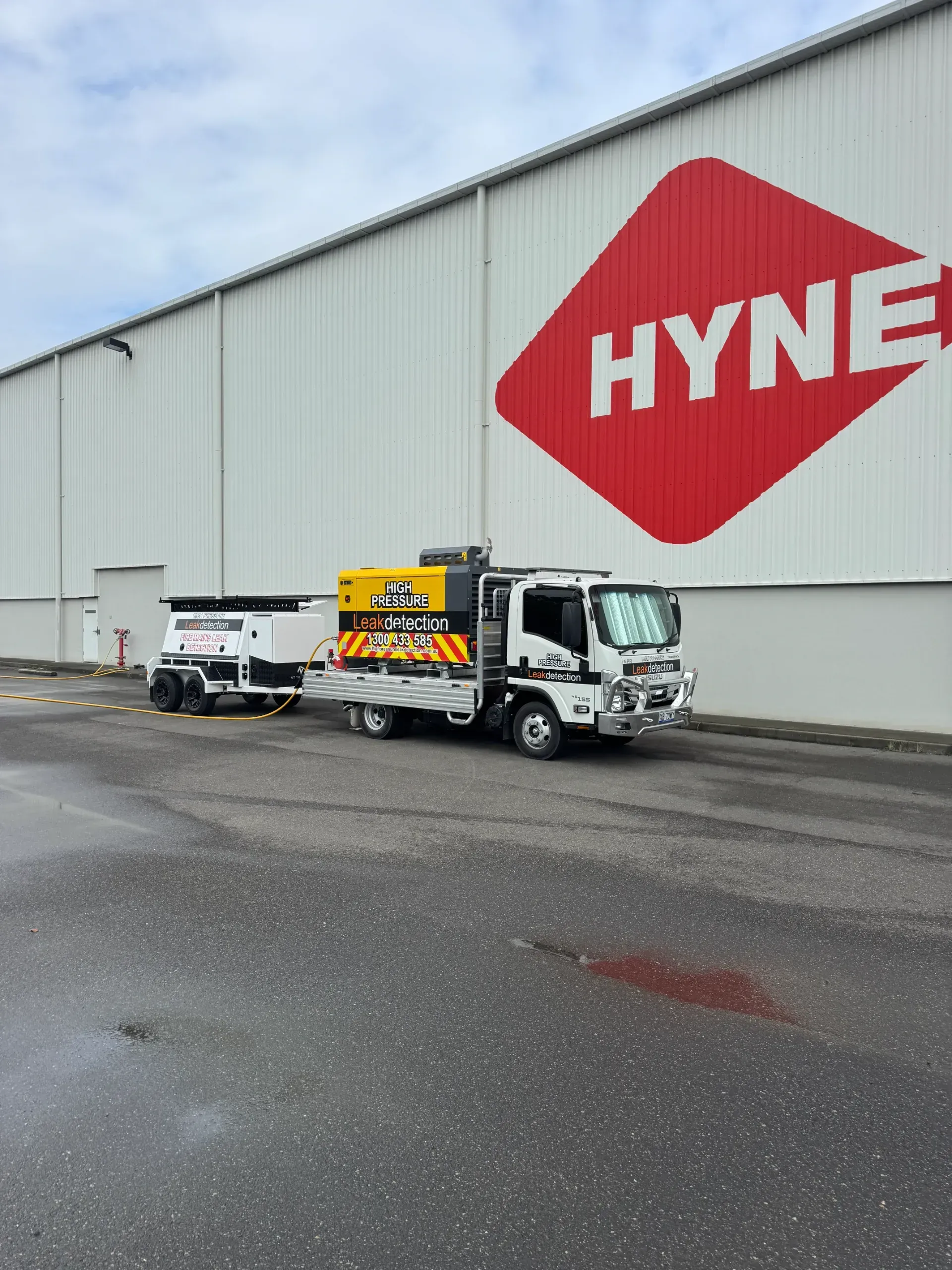 Truck with trailer parked in front of a Hyne building with a red and white logo.  — Commercial Leak Detection