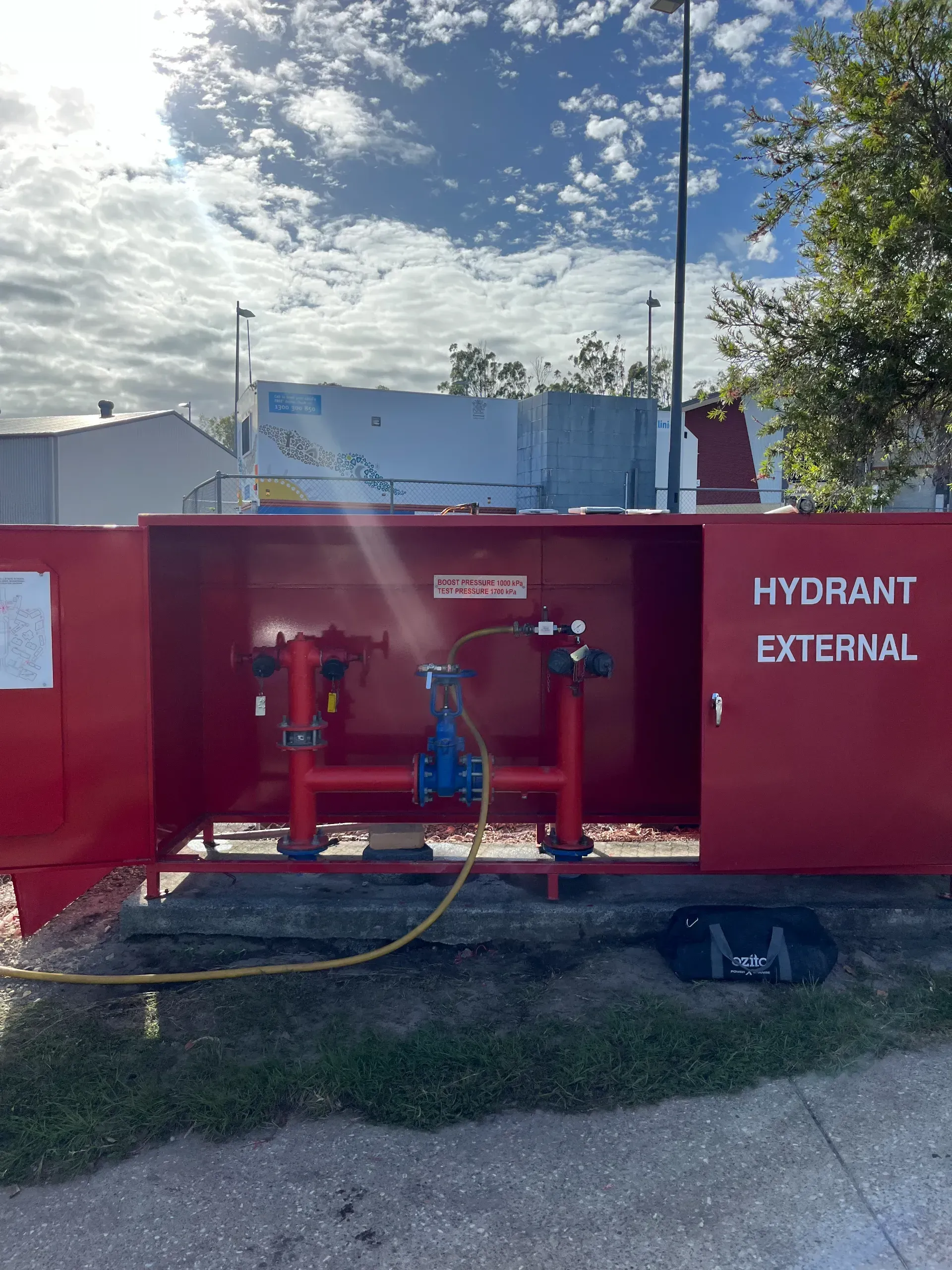 Red fire hydrant cabinet with open doors; water hose connected, blue sky background.  — Commercial Leak Detection