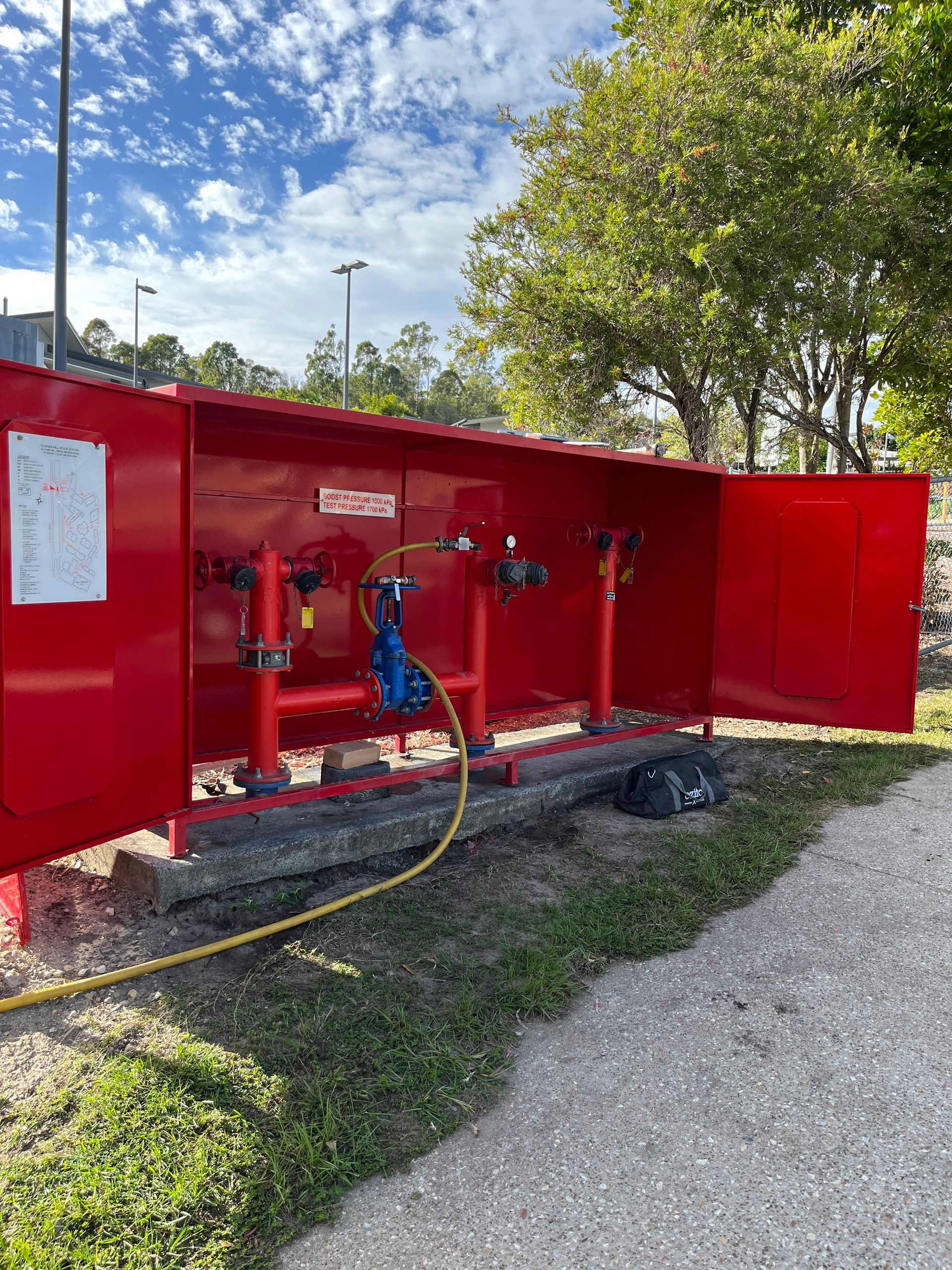 Red fire hydrant cabinet outdoors with open doors. A hose is connected, and a white sign is visible.