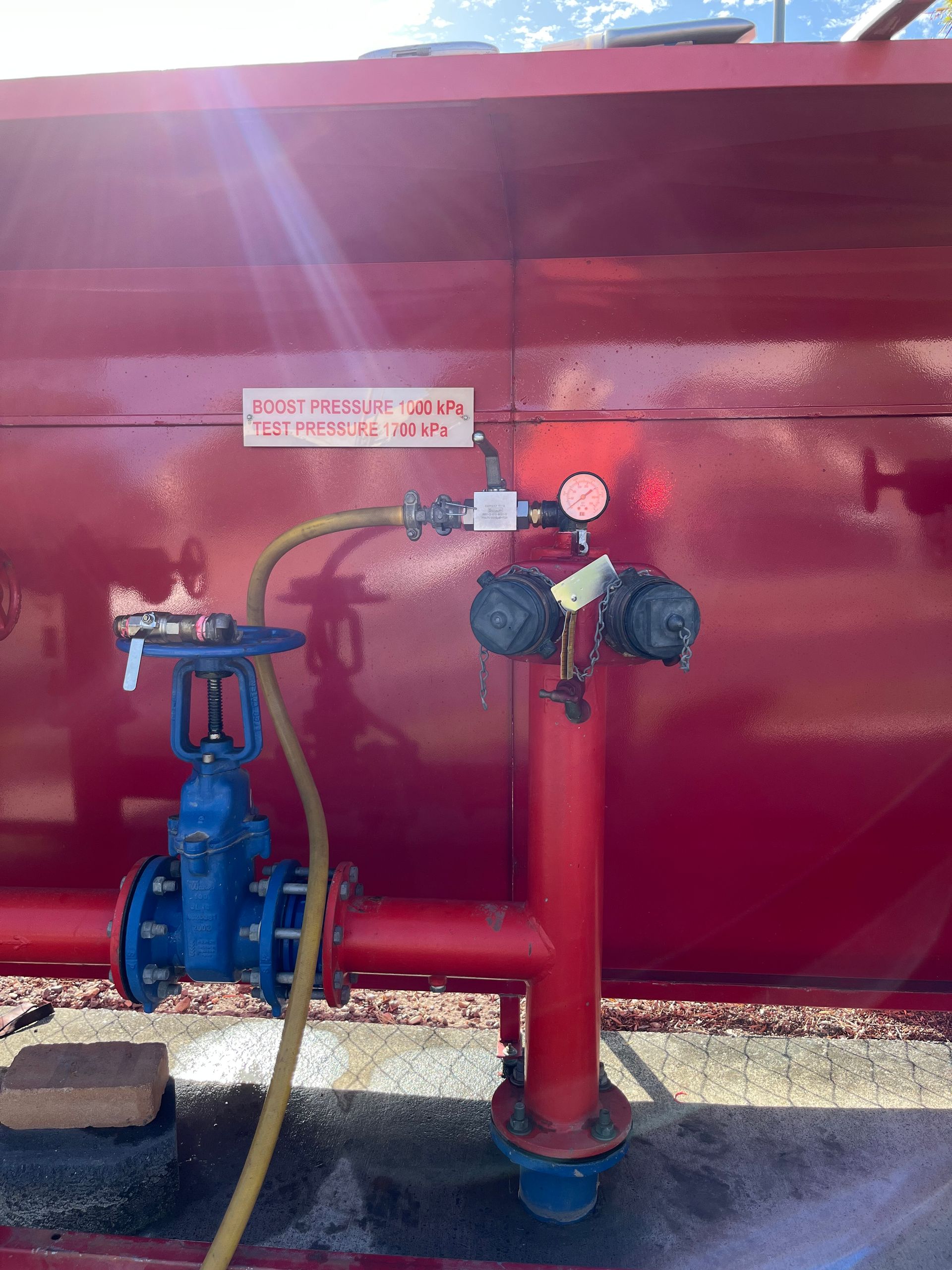 Red tank with blue valve, hose, and red pipes. Signs and gauges present.