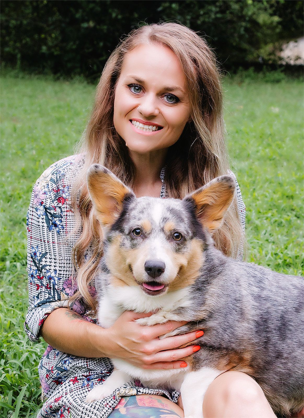A woman is sitting in the grass holding a dog.