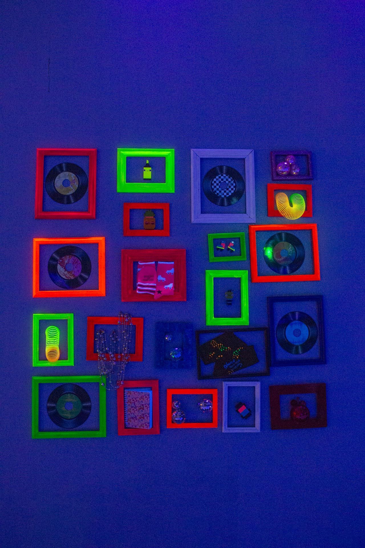 Arrangement of framed art with neon frames on a dark blue wall, lit with ultraviolet light.