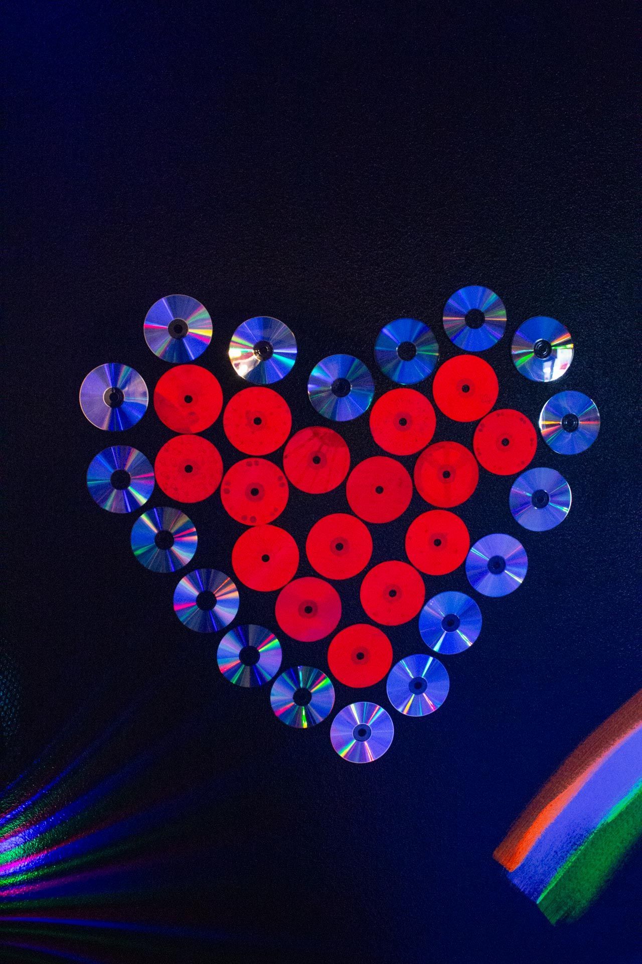 Heart made of red and blue CDs on a black background with a rainbow in the corner.
