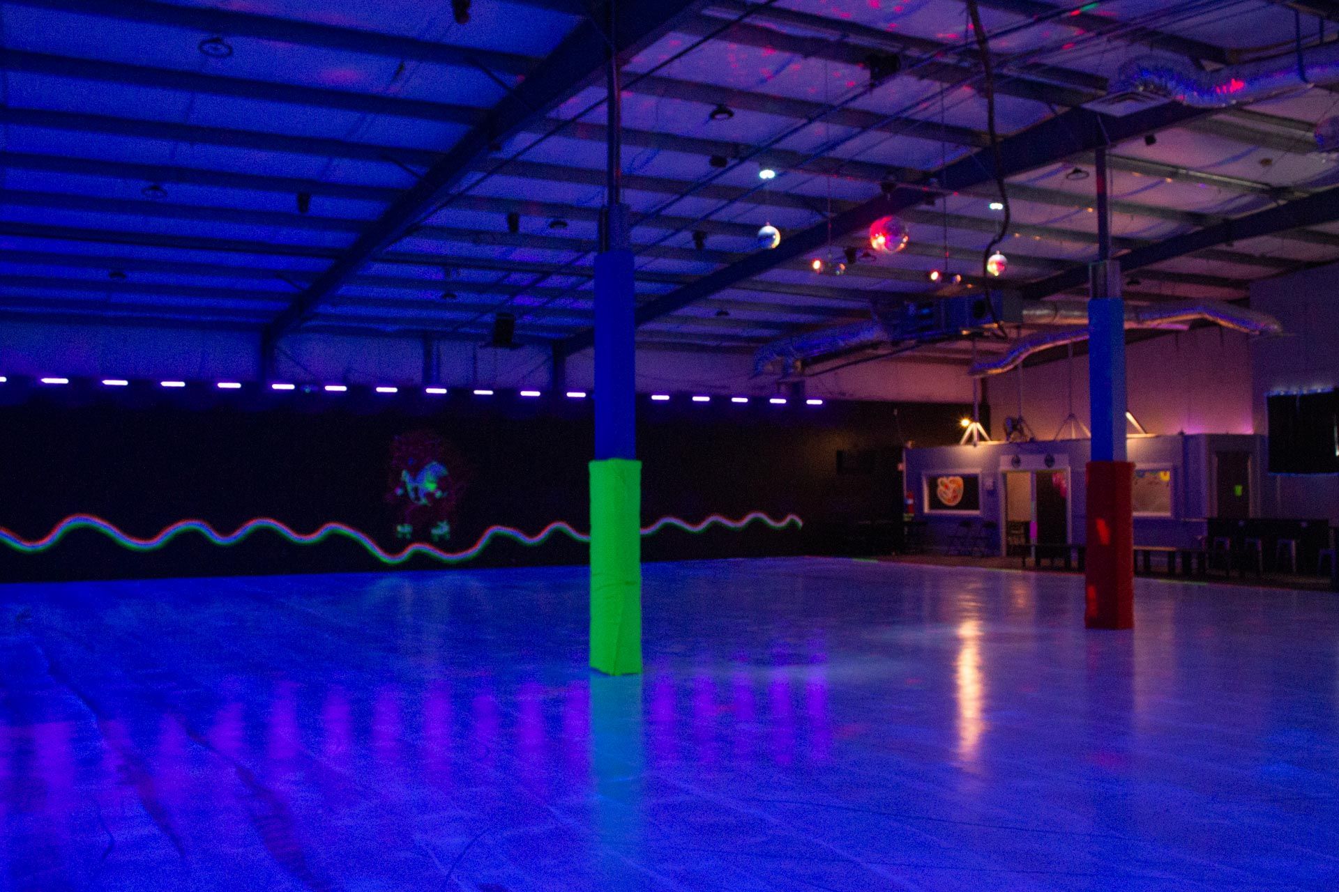Empty roller skating rink with black lights; blue and green pillars; black wall with neon wave design.