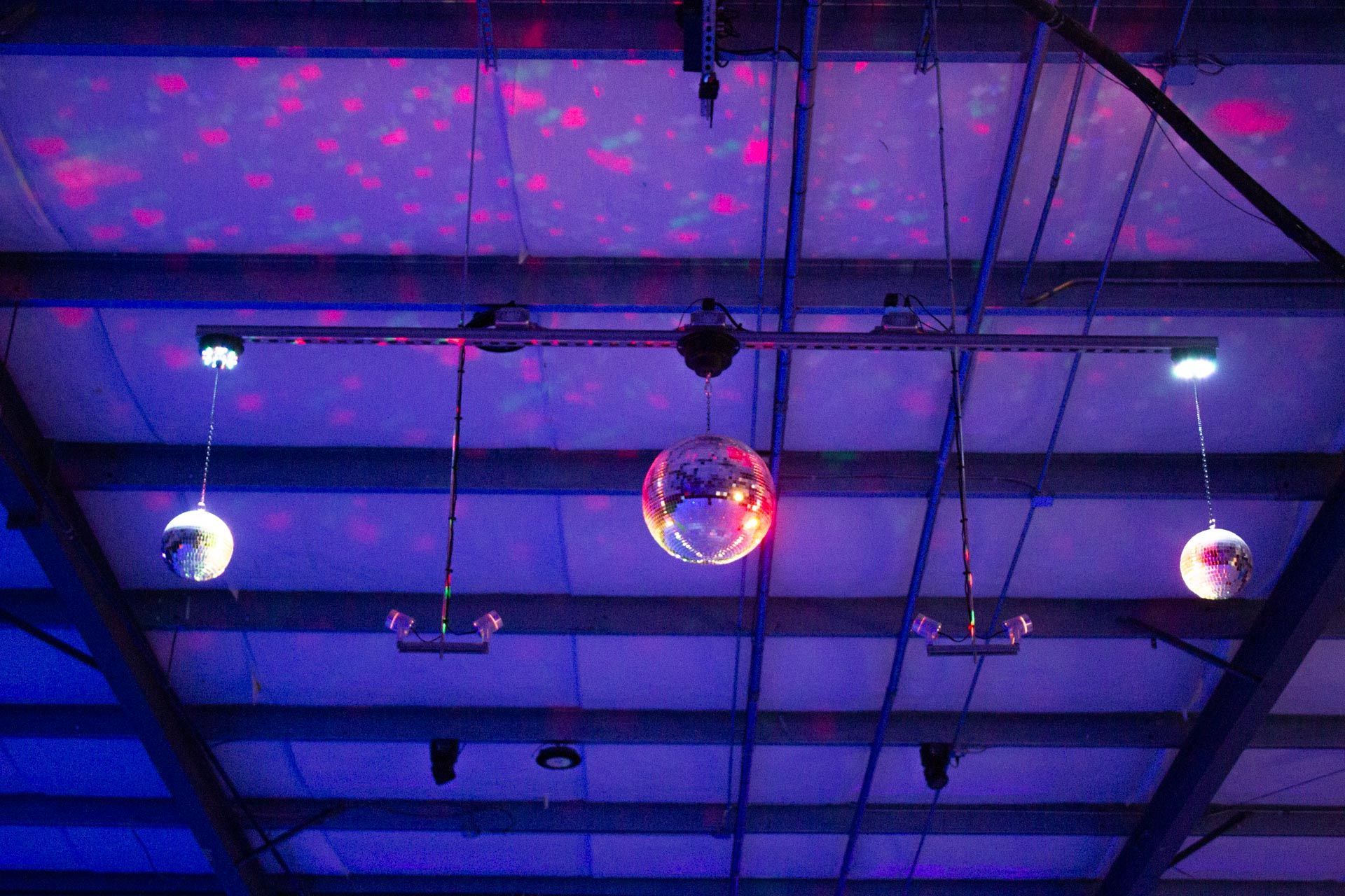 Disco balls hanging from a ceiling with colorful lights in a dark room.