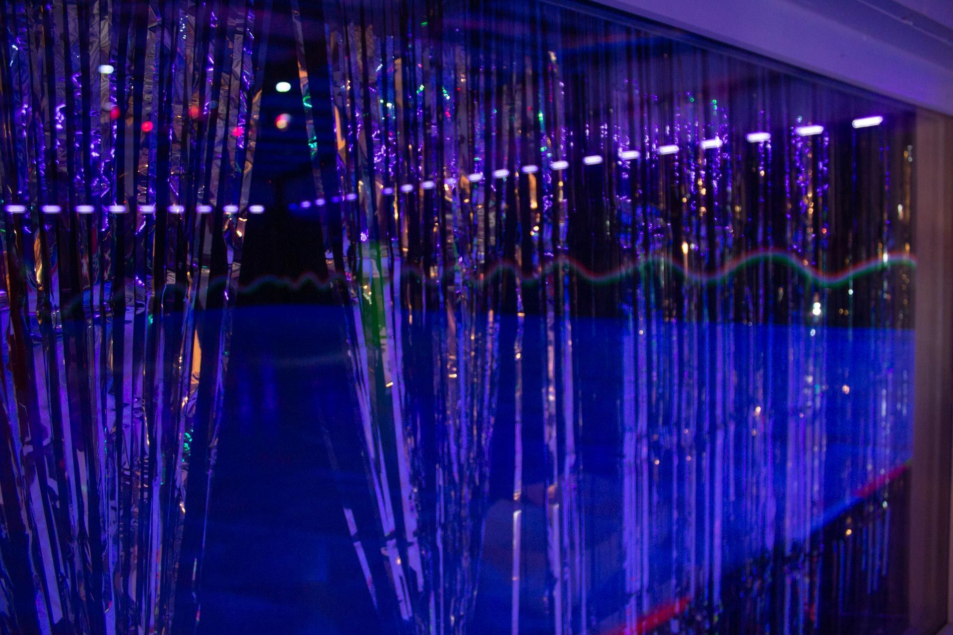 Blue-lit tinsel curtain partially obscuring a room with colored lights, creating a party atmosphere.