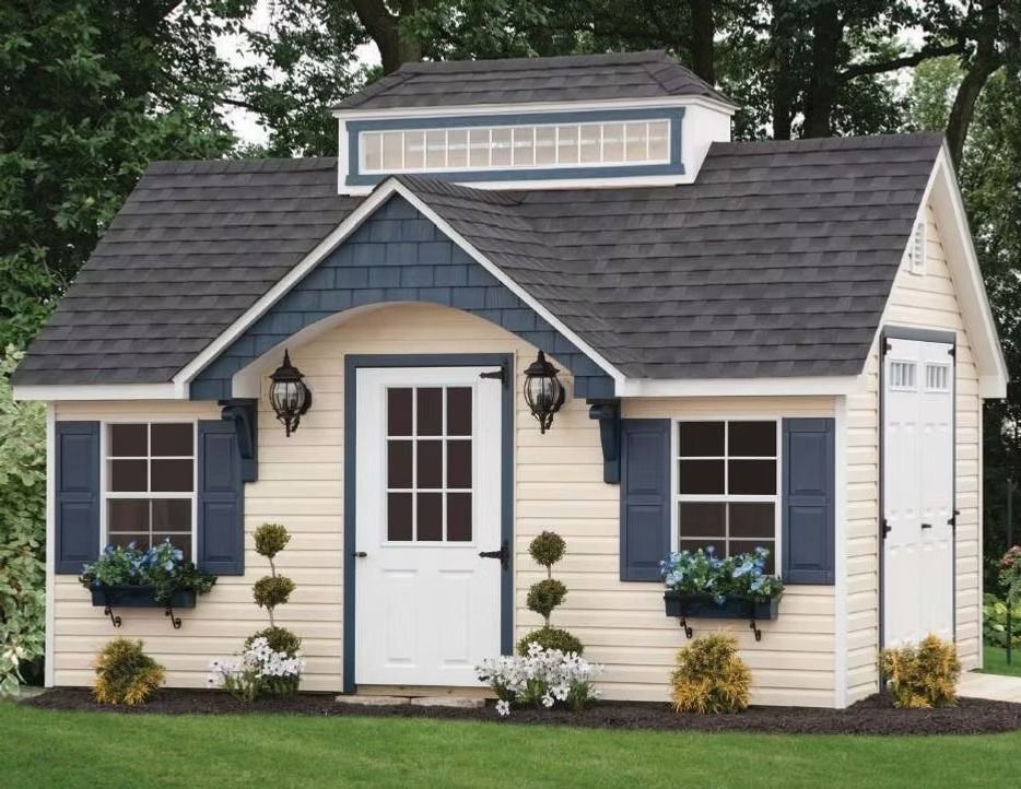 Small beige cottage with dark roof, white door, blue shutters, and flower boxes