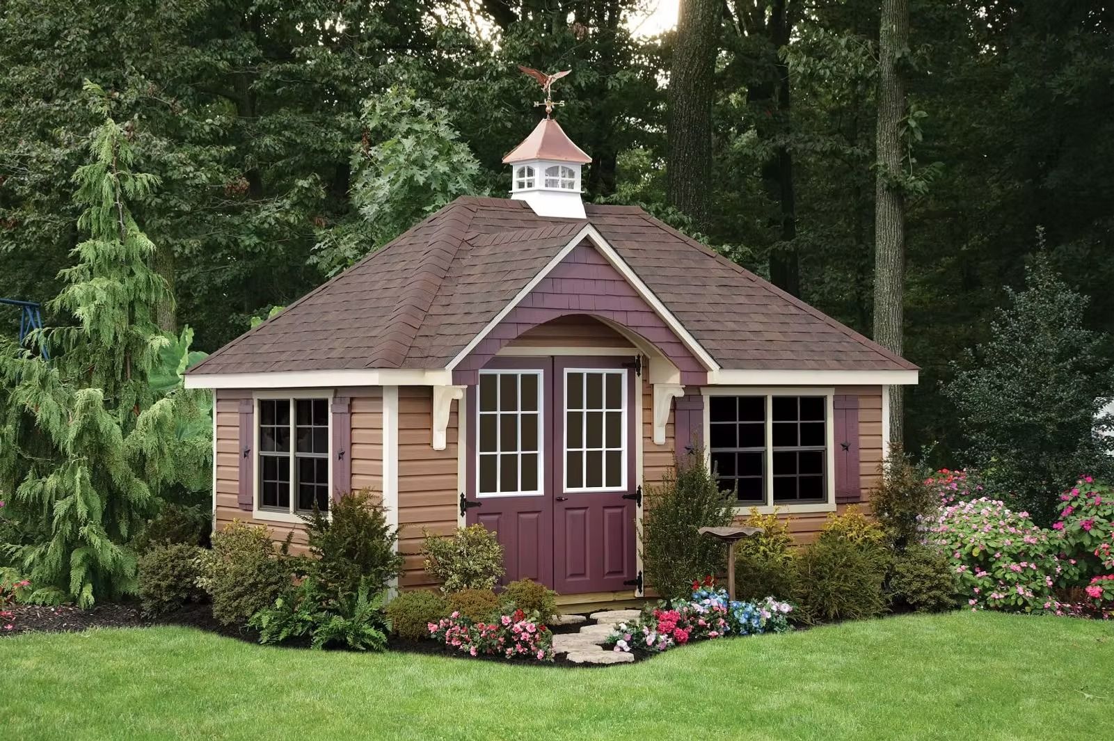 Small purple garden gazebo with white-trimmed windows and flowers, surrounded by trees and lawn