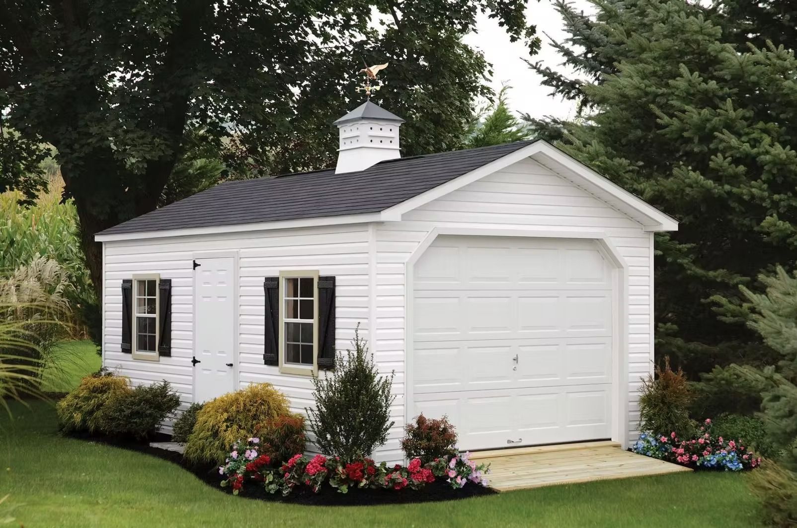 White detached garage with black roof, white door, and flower beds in a green yard.