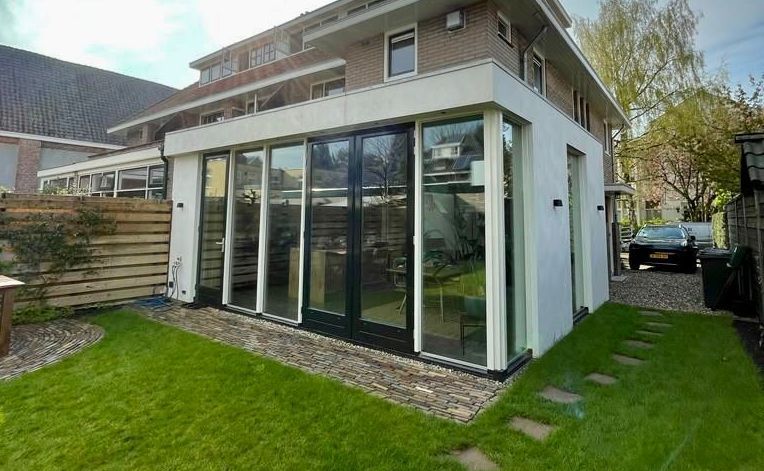 Een groot huis met veel ramen en een auto ervoor geparkeerd.