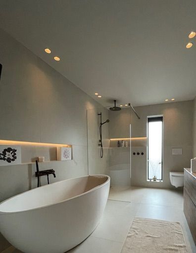 Een badkamer met bad, toilet, douche en raam.