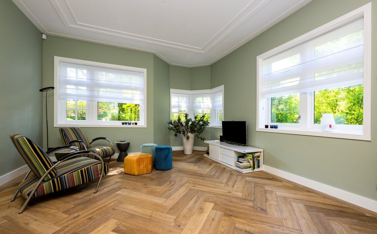 Een woonkamer met een houten vloer, stoelen, voetenbankjes en een televisie.