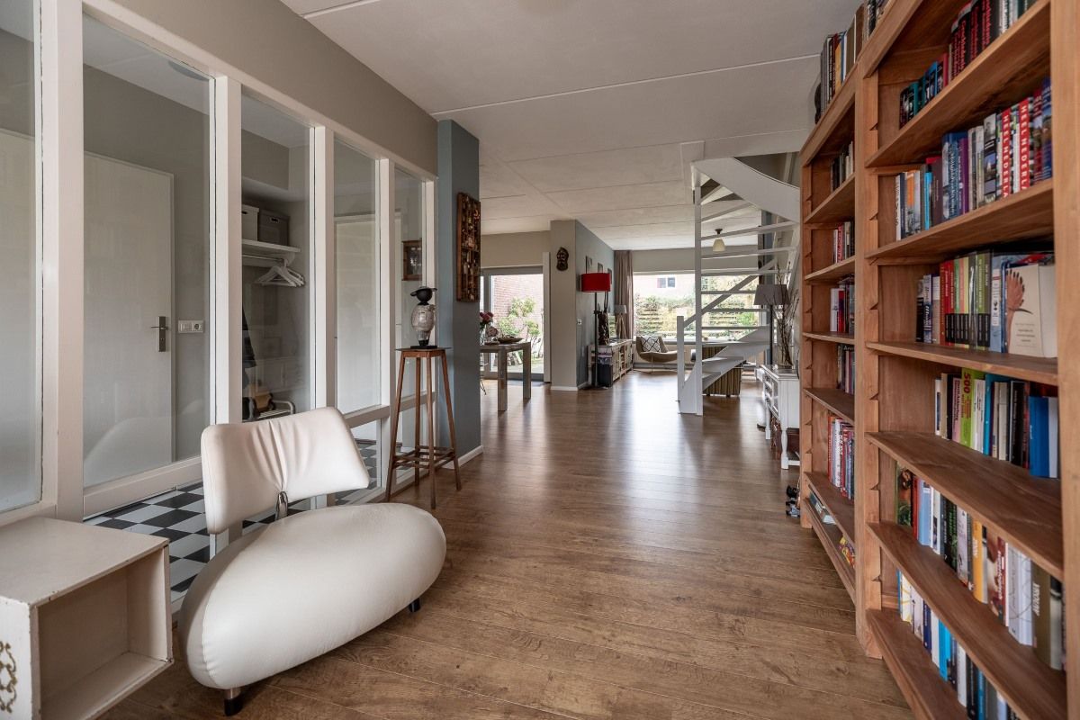 Een witte stoel staat in een gang naast een boekenkast vol boeken.