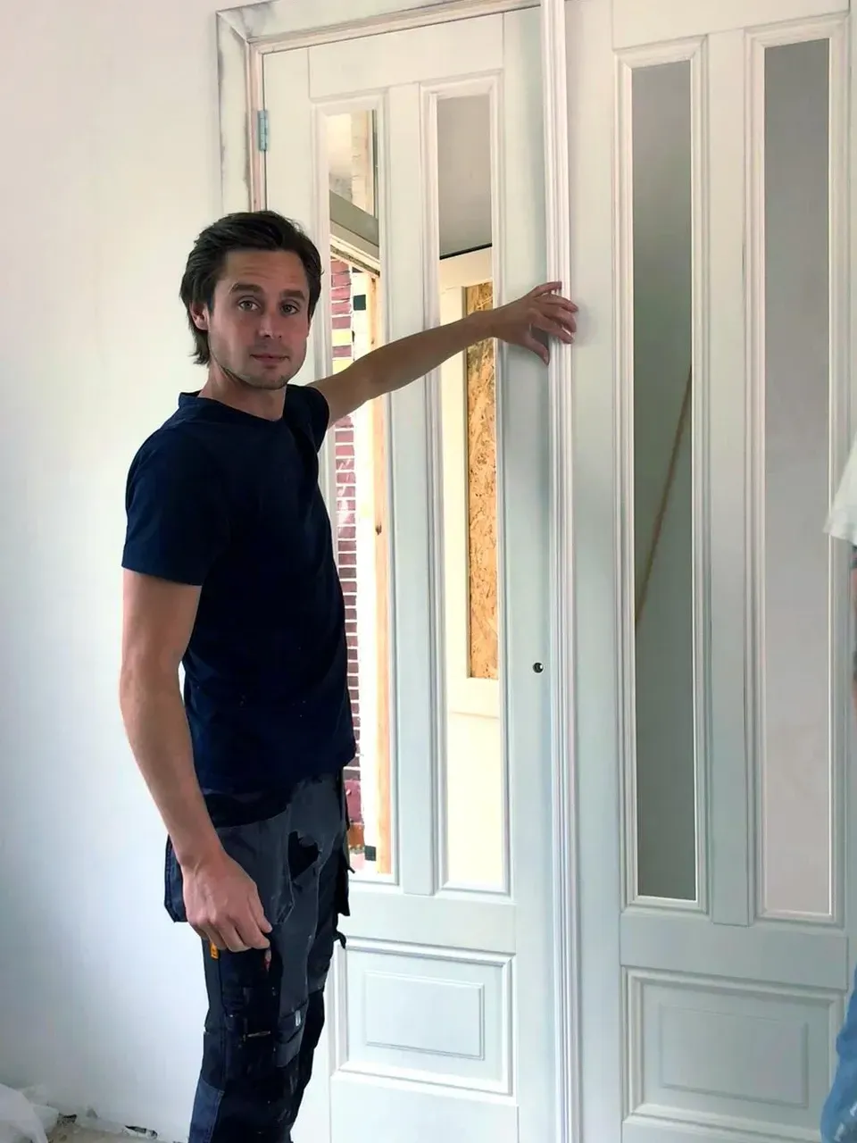 Een man in een blauw shirt staat voor een witte deur.