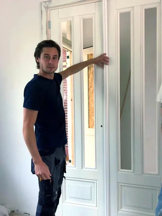 Een man in een blauw shirt staat voor een witte deur.