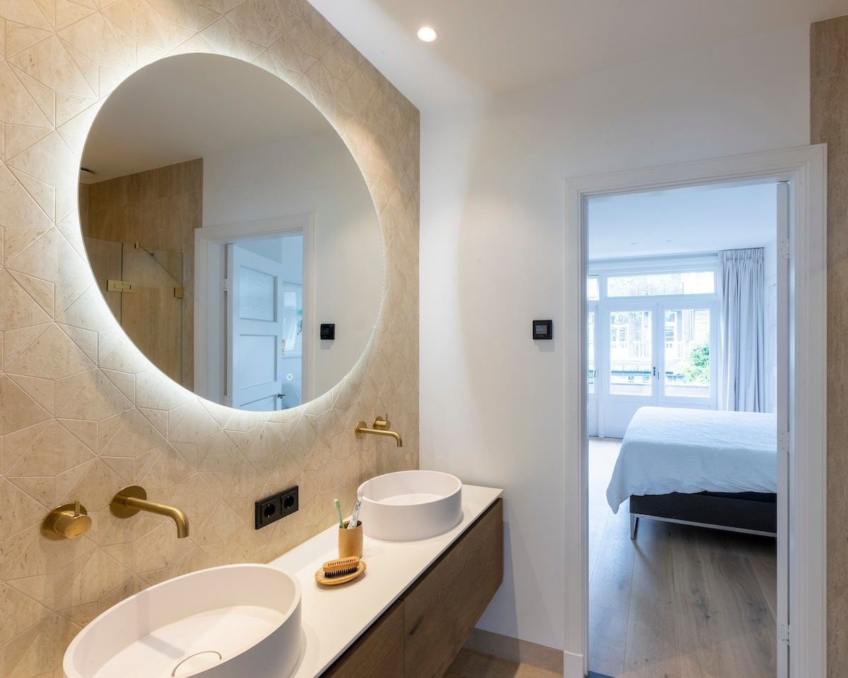 Een badkamer met twee wastafels en een ronde spiegel.