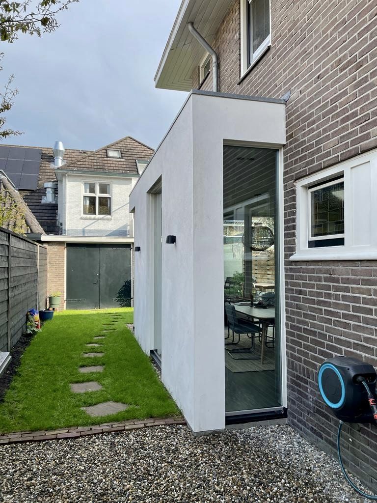 Een bakstenen huis met een witte uitbouw aan de zijkant.