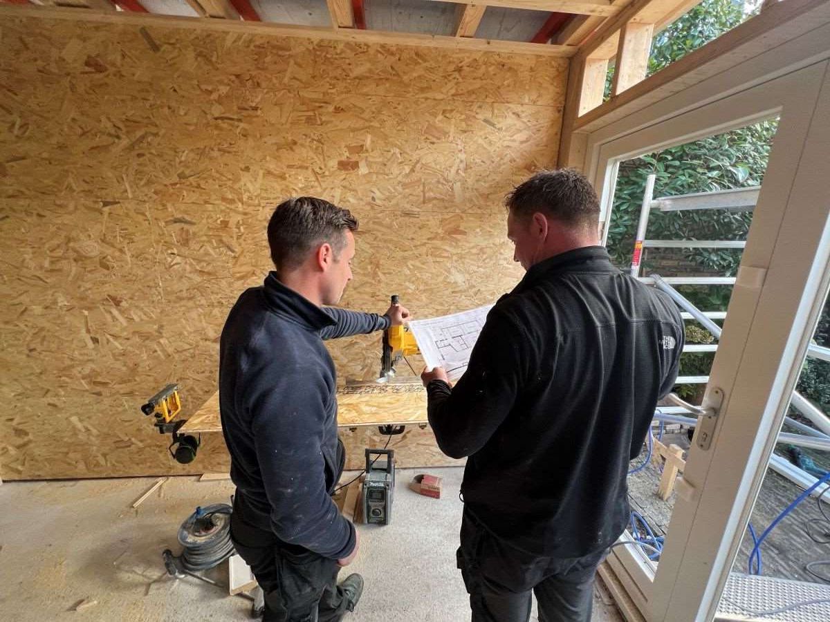 Een timmerman meet een stuk hout met een rolmaat.