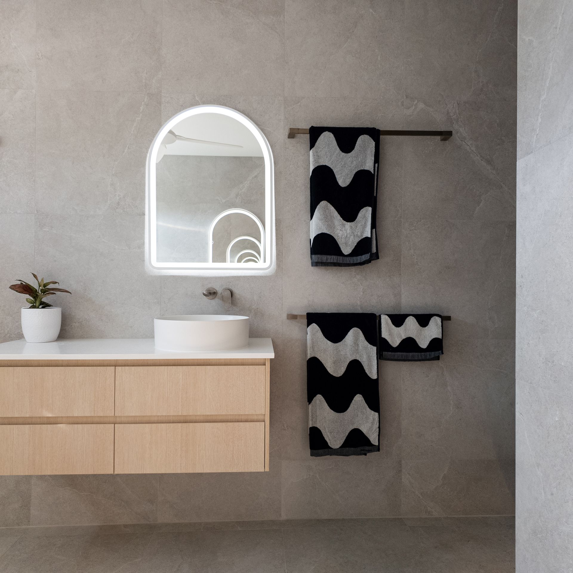Bathroom vanity with curved mirror, timber cabinetry and textured tiles