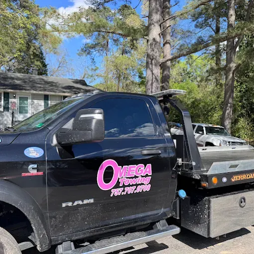 Black Omega Towing truck with pink logo parked near a house and trees.
