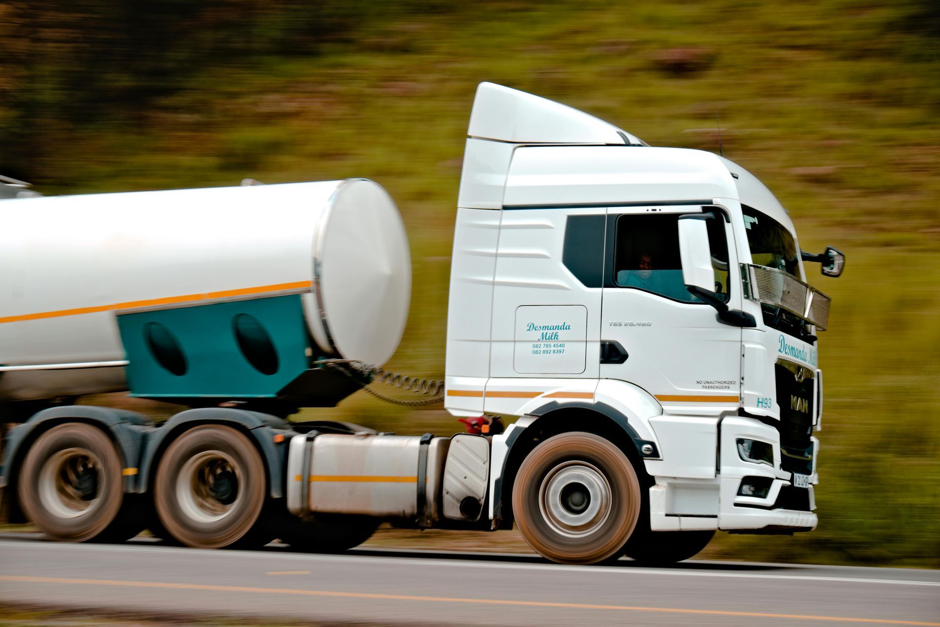 White tanker truck driving on a road, blurred background, teal and yellow details.