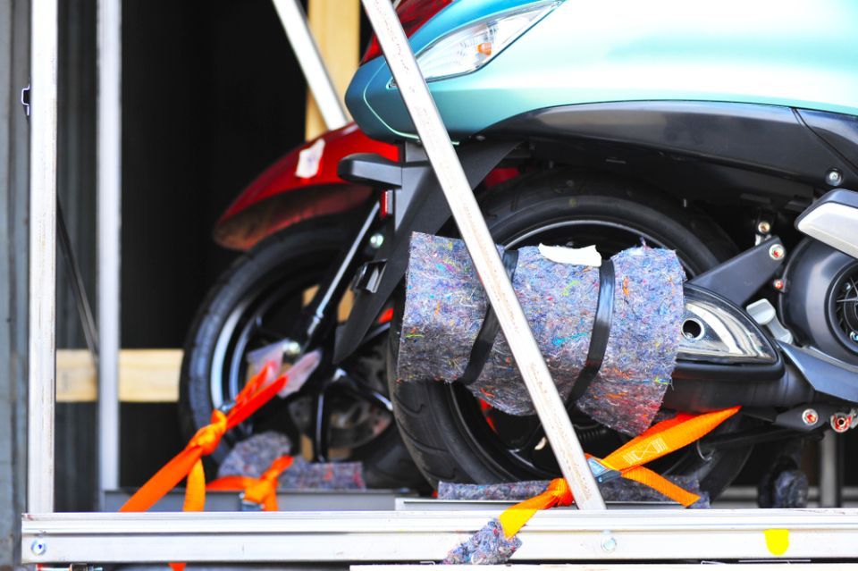 Scooter secured in a shipping crate with straps and padding, close-up of rear wheel and fender.