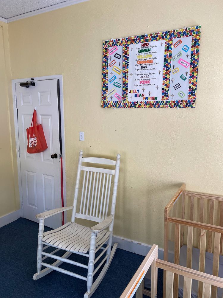 A white rocking chair is sitting in a room next to a crib.