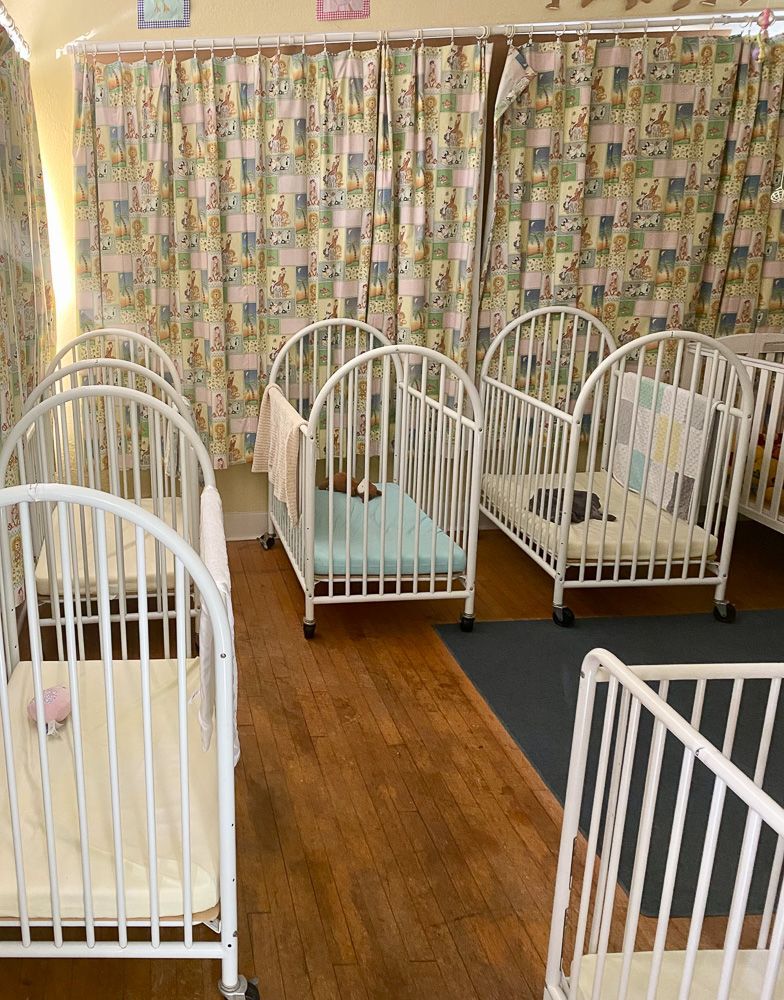 A row of white cribs are lined up in a room.